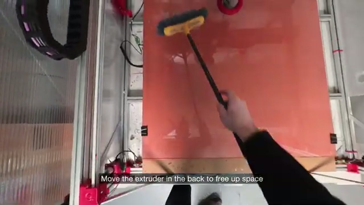 Scraping the glass bed with a yellow squeegee to remove print residue