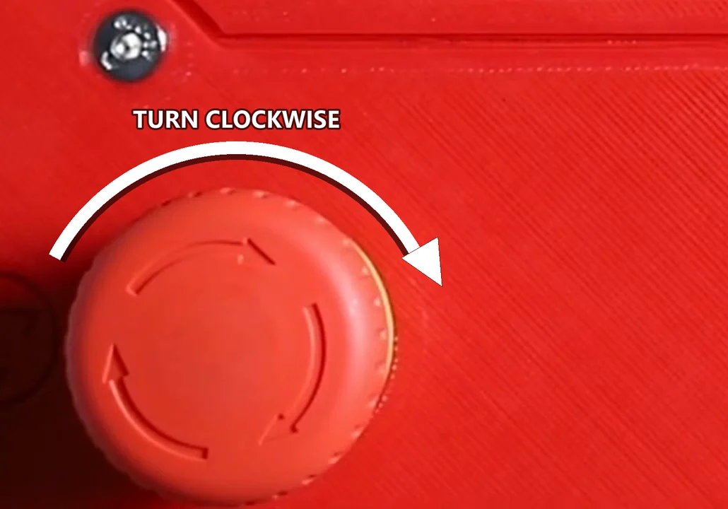 The emergency stop button on the G1's front panel, a white arrow drawn over it curving clockwise to show the direction that releases it