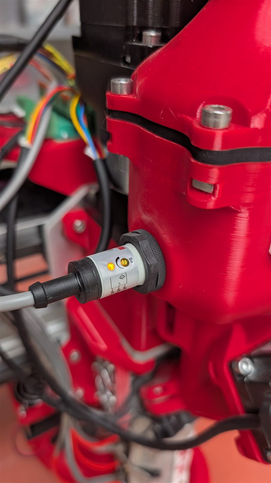 The capacitive level probe threaded into the side of the red hopper body, its cable running away to the left