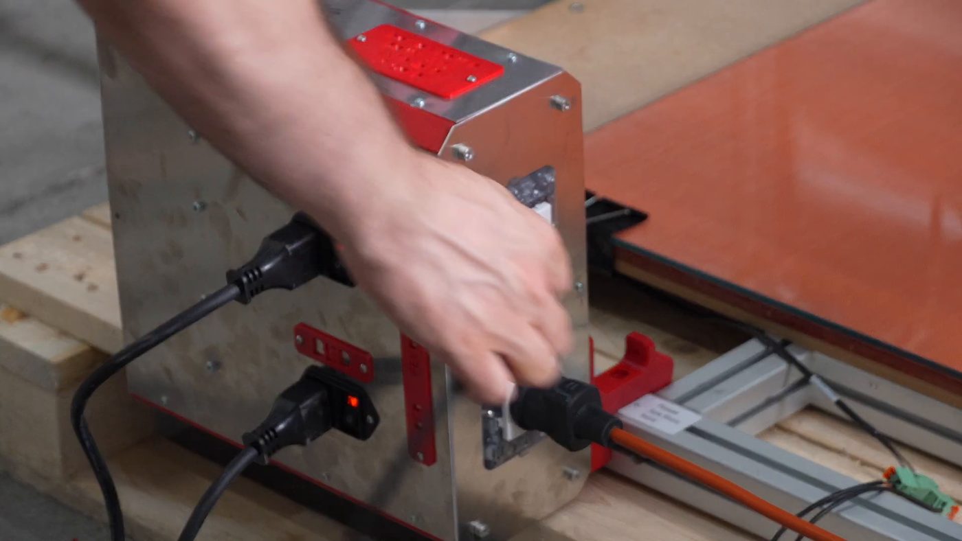 The vacuum being plugged into the power box during assembly, the box sitting on the shipping crate with two switched inlets lit red on its left face